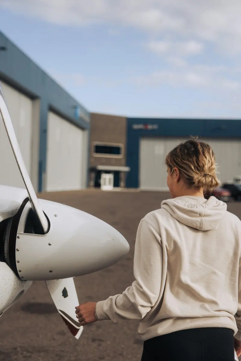 Pilotin prüft beim Außencheck mit der Hand den Propeller eines weißen Tiefdeckers